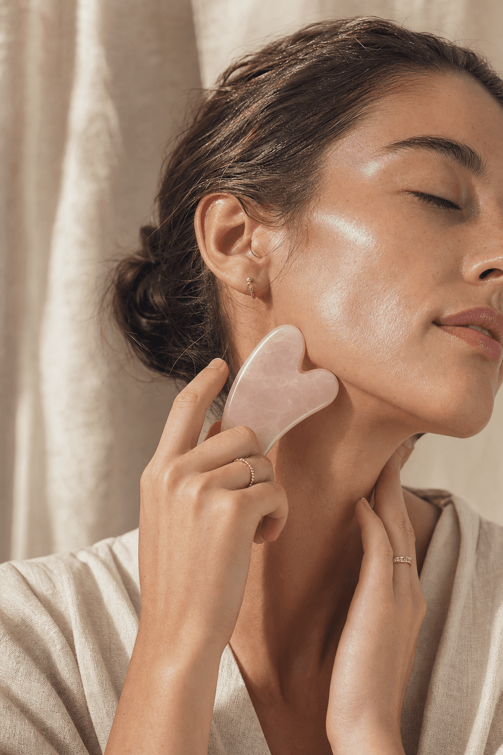 Hands holding rose quartz gua sha in soft morning light